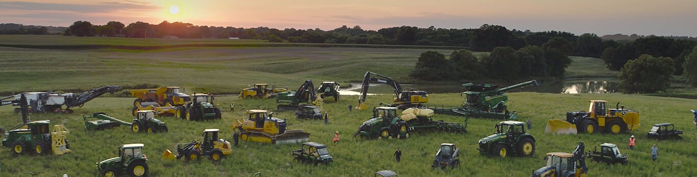 Ljudi razgledaju nekoliko tipova opreme kompanije John Deere u velikom polju.