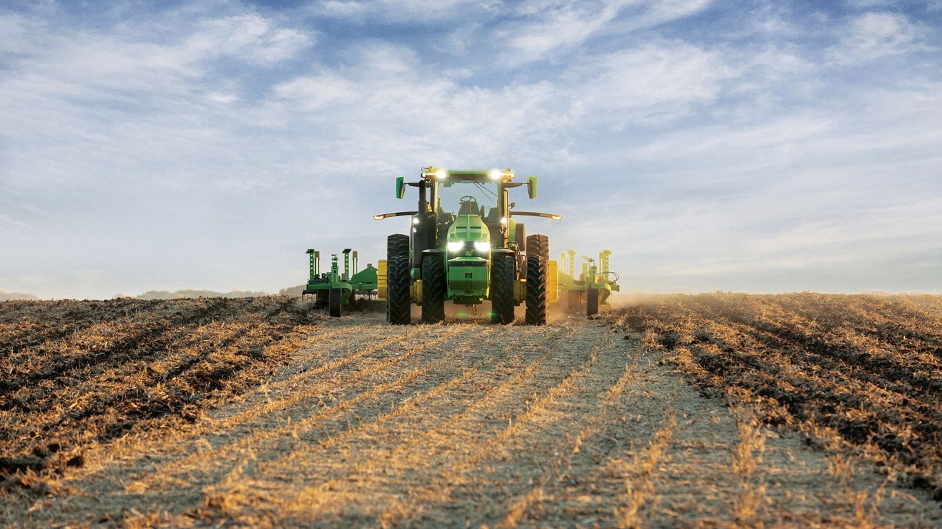 Samohodni John Deere traktor vuče opremu za obradu zemlje kroz otvoreno polje.