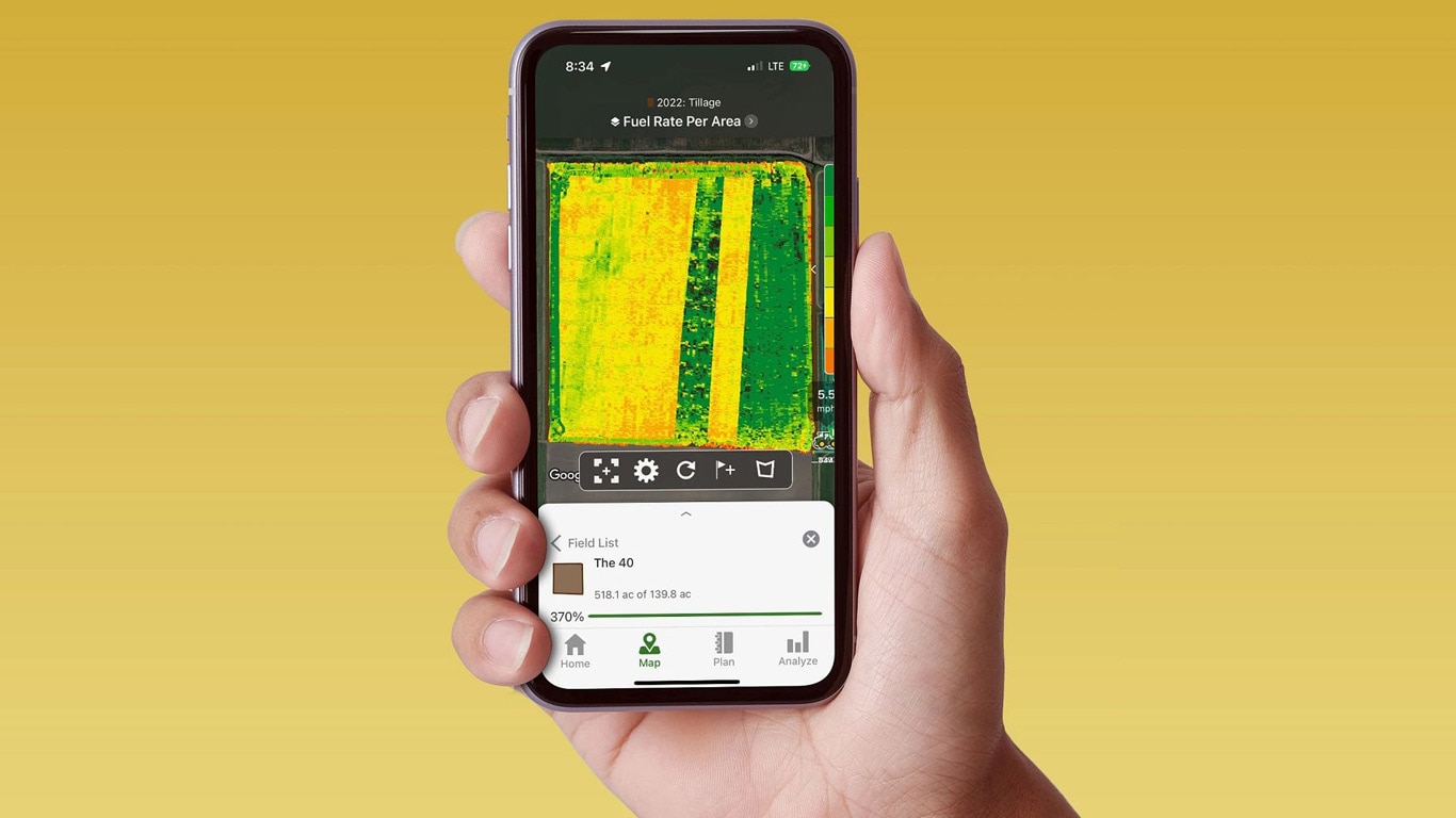 Ruka s pametnim telefonom na čijem ekranu je prikazan John Deere Operations Center s podacima o protoku goriva.