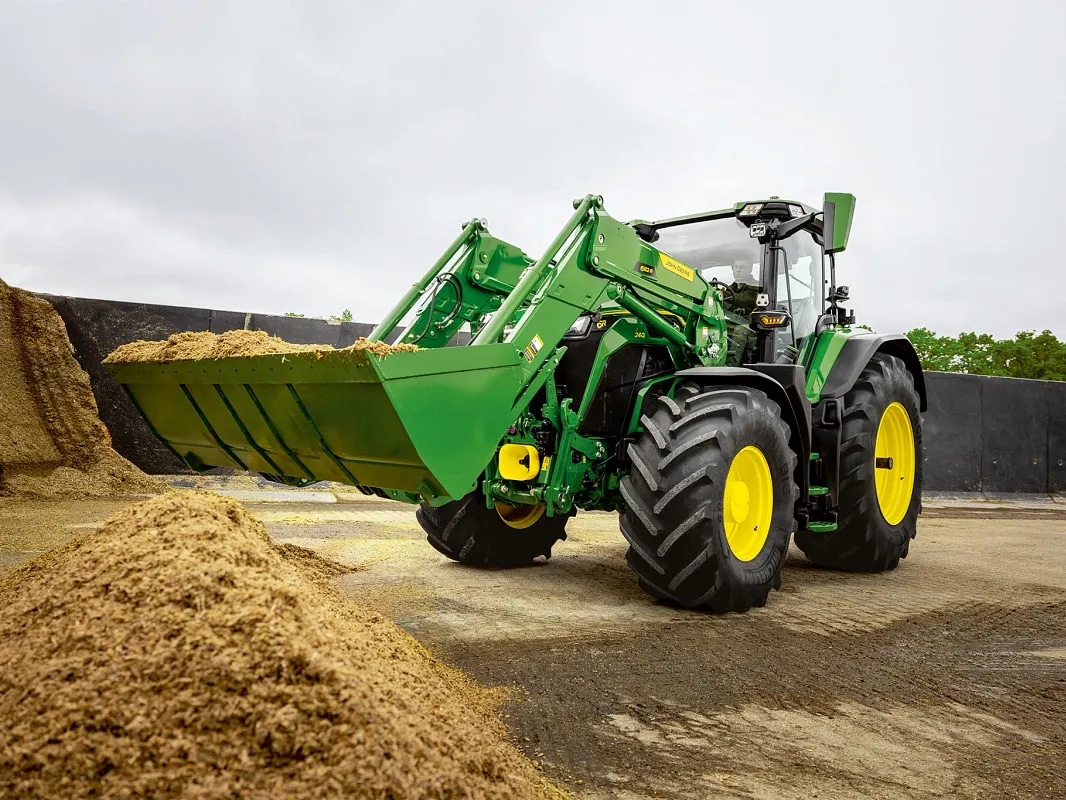 Kašika prednjeg utovarivača ispunjena silažom na traktoru John Deere tokom rada na rukovanju materijalom.