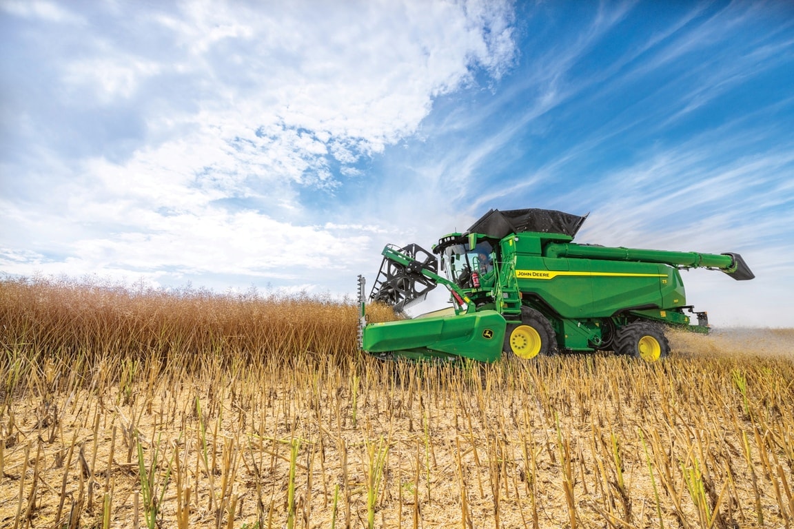 John Deere kombajn žanje pšenicu hederom u polju pod plavim nebom tokom žetve