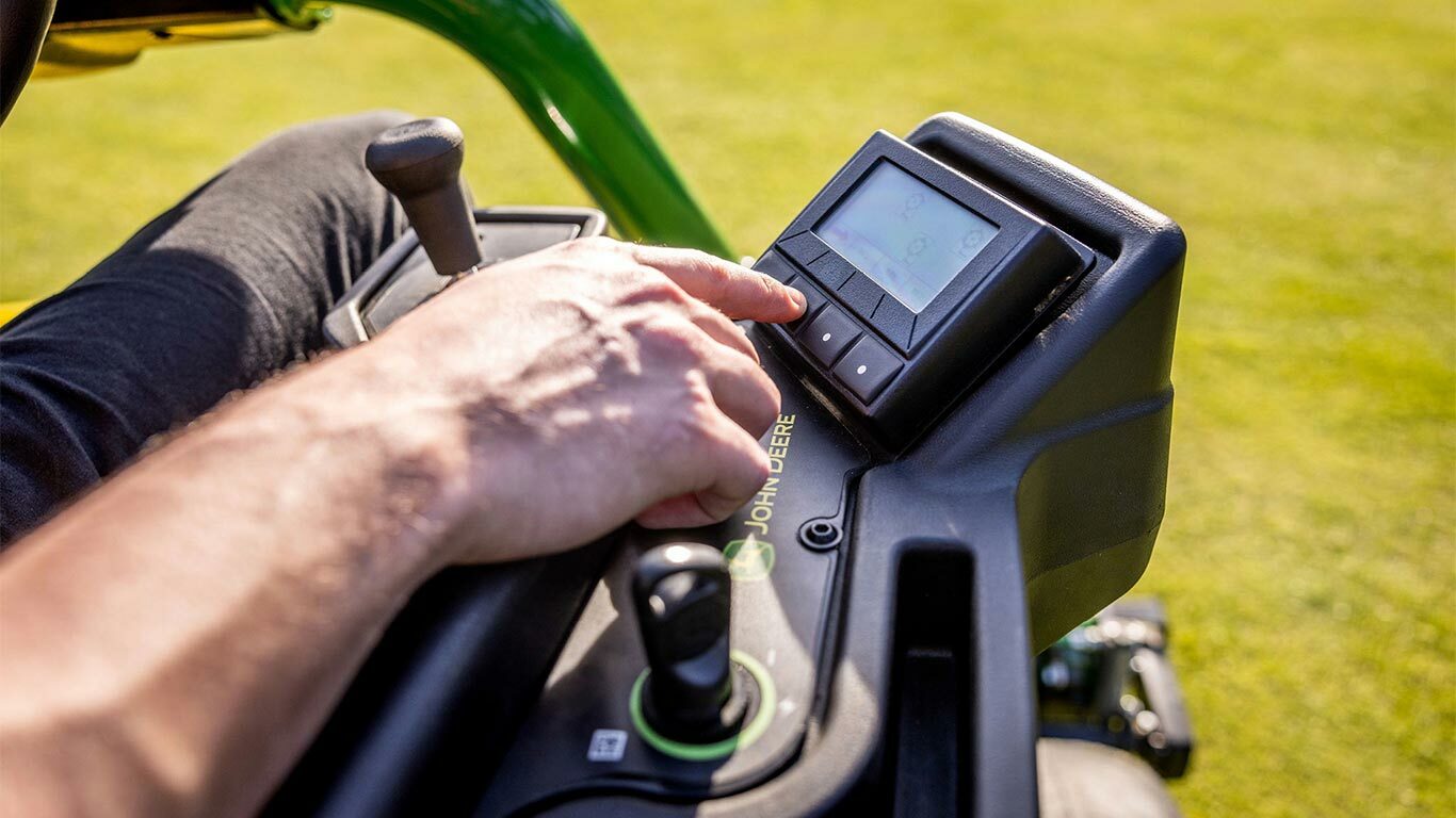 Uvećani prikaz ruke čoveka koji koristi TechControl panel na John Deere 2775 E-Cut™ Electric kosačici i pritiska dugmad na digitalnom ekranu, dok se vide džojstik i druge kontrole.