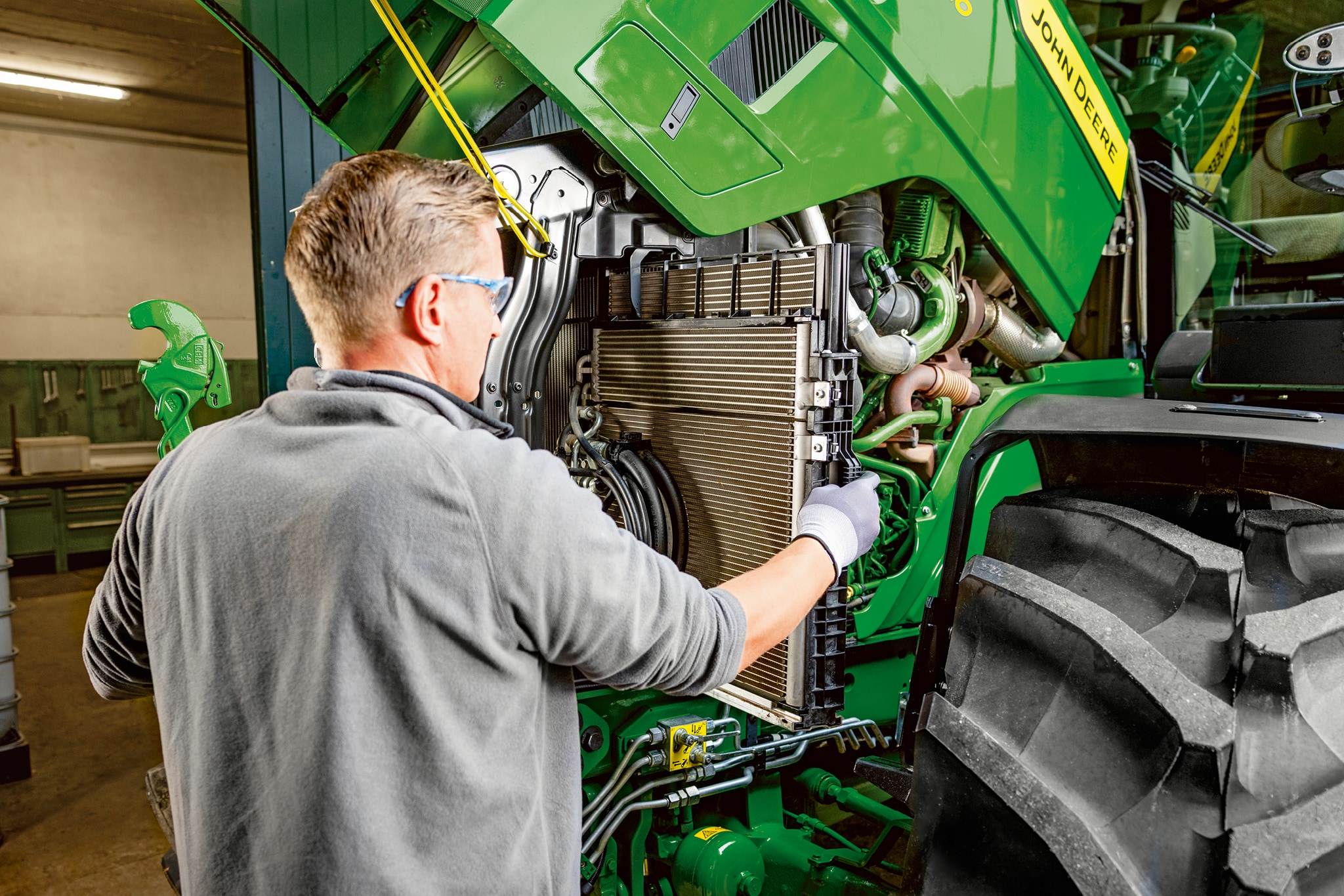 Serviser koji vrši održavanje unutar odeljka motora traktora John Deere serije 6M.