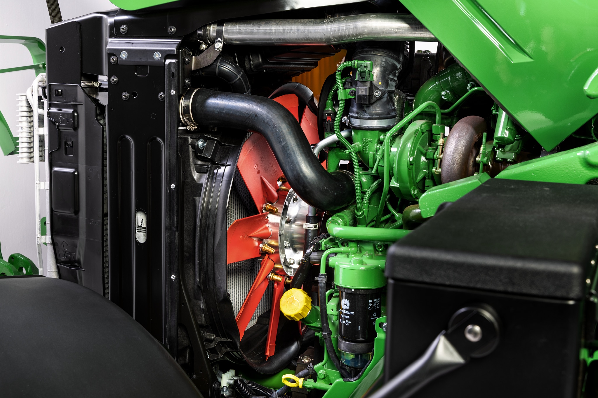 Pogled izbliza na motorni odeljak serije John Deere 6M koji ističe sistem hlađenja i komponente motora.