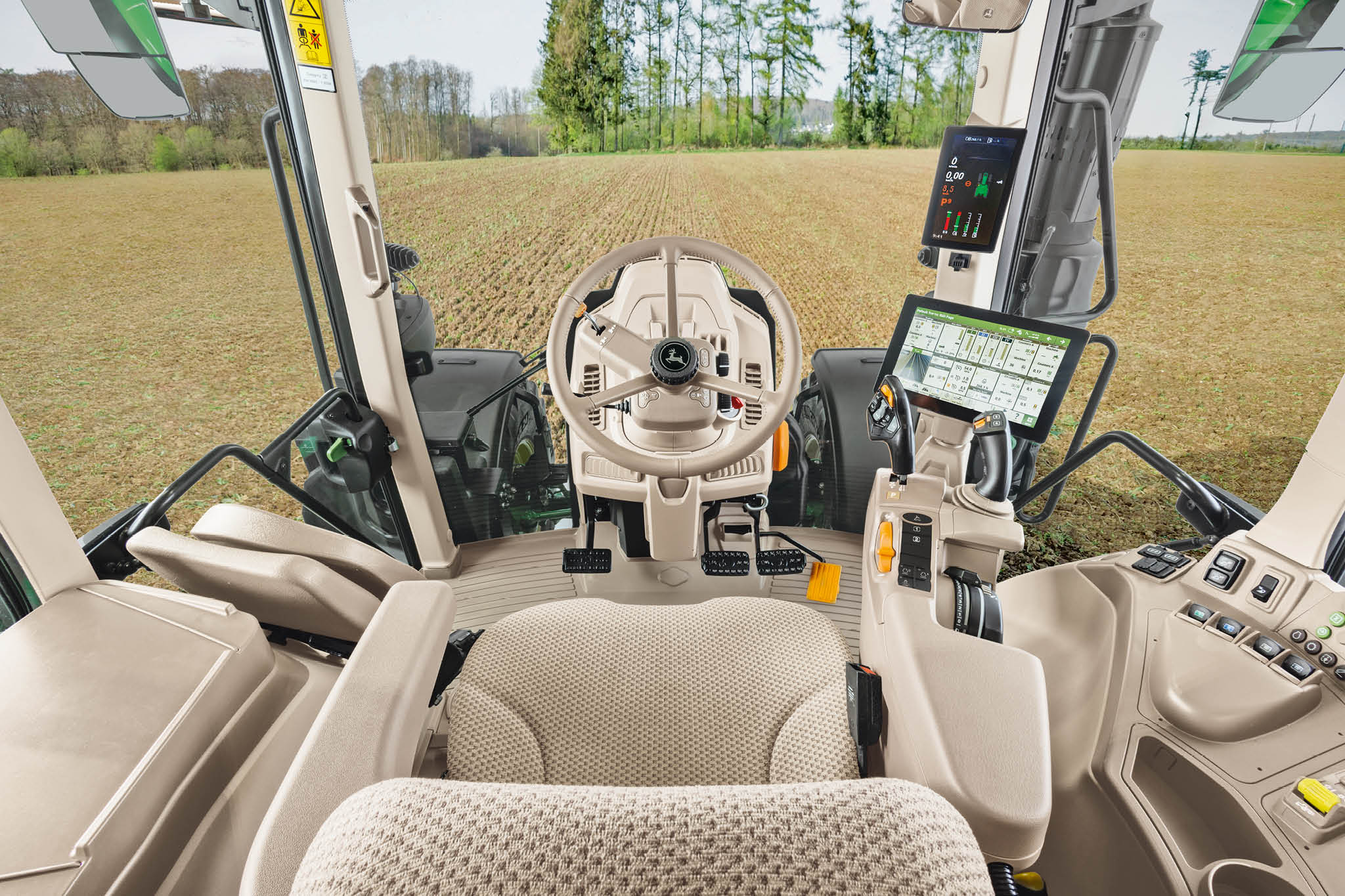 Pregled unutrašnjosti traktorske kabine serije John Deere 6M sa sedištem rukovaoca, volanom i digitalnim ekranima.
