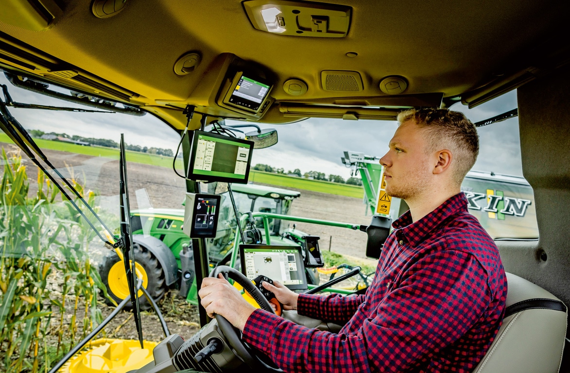 Farmer upravlja naprednim poljoprivrednim mašinama preko nekoliko digitalnih ekrana u kabini samohodnog silažnog kombajna i prikazuje savremenu poljoprivrednu tehnologiju na polju.
