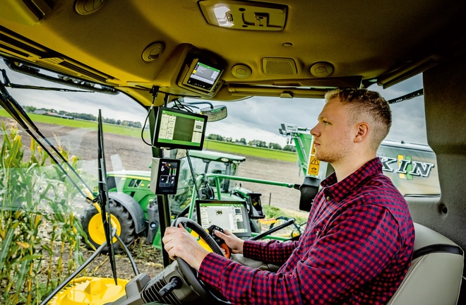 Farmer upravlja naprednim poljoprivrednim mašinama preko nekoliko digitalnih ekrana u kabini samohodnog silažnog kombajna i prikazuje savremenu poljoprivrednu tehnologiju na polju.
