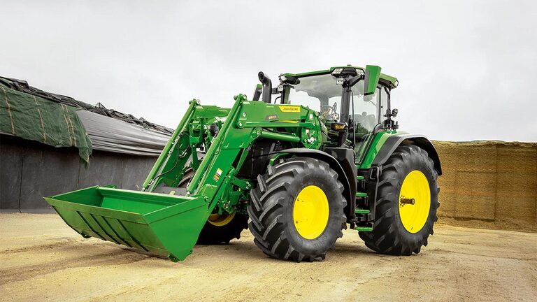 John Deere traktor sa prednjim utovarivačem parkiranim na površini poljoprivrednog gazdinstva u blizini skladišta silaže.