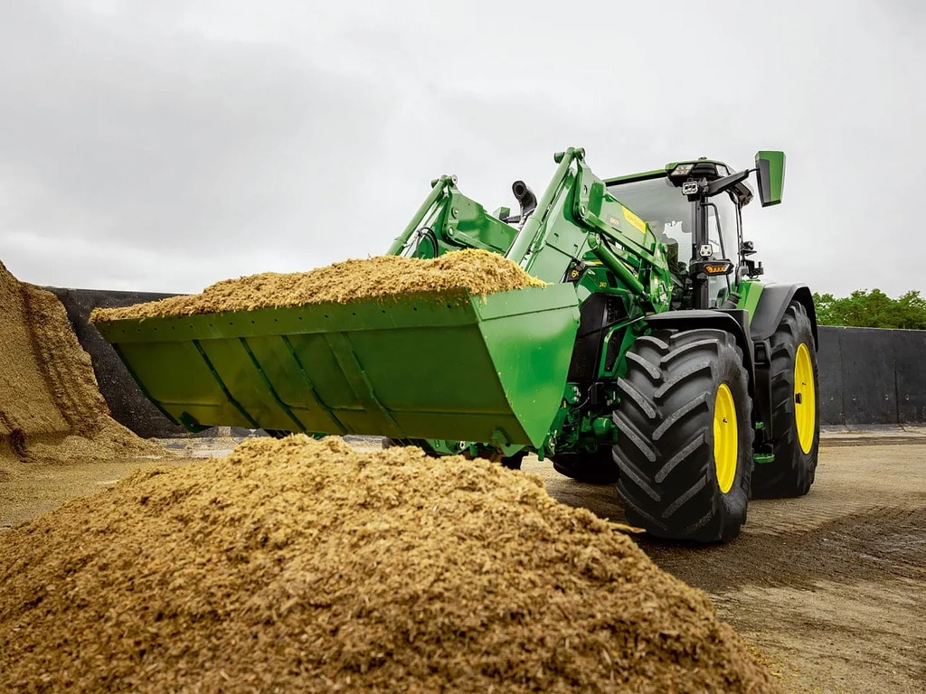 Traktor John Deere koristi prednji utovarivač za prenos usitnjene silaže u prostoru za skladištenje poljoprivrednih proizvoda.