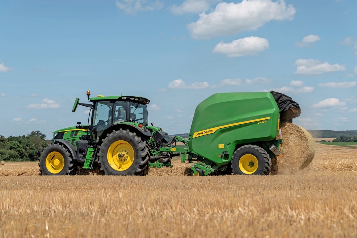 John Deere V452R na polju sa slamom koju vuče John Deere 6R 150 izbacuje balu