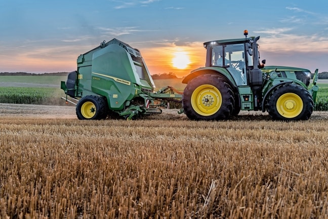 John Deere V462M na polju sa slamom koju vuče John Deere 6M 150 u zalazak sunca