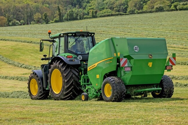 John Deere F442M balirka koju vuče traktor John Deere 6M na brdovitom polju trave