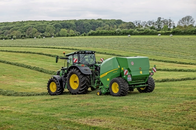 John Deere F442R balirka koju vuče traktor John Deere 6M na brdovitom polju trave